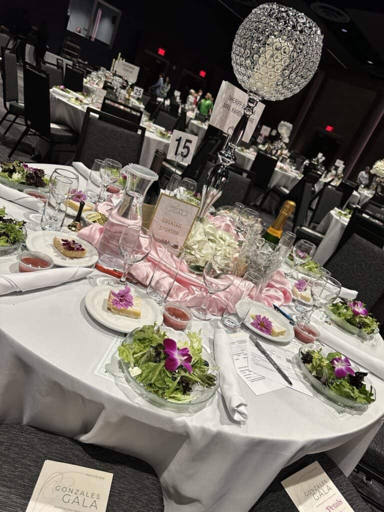 A round banquet table set for the Gonzales Gala with salads, drinks, menus, and a decorative crystal centerpiece, labeled table 15.