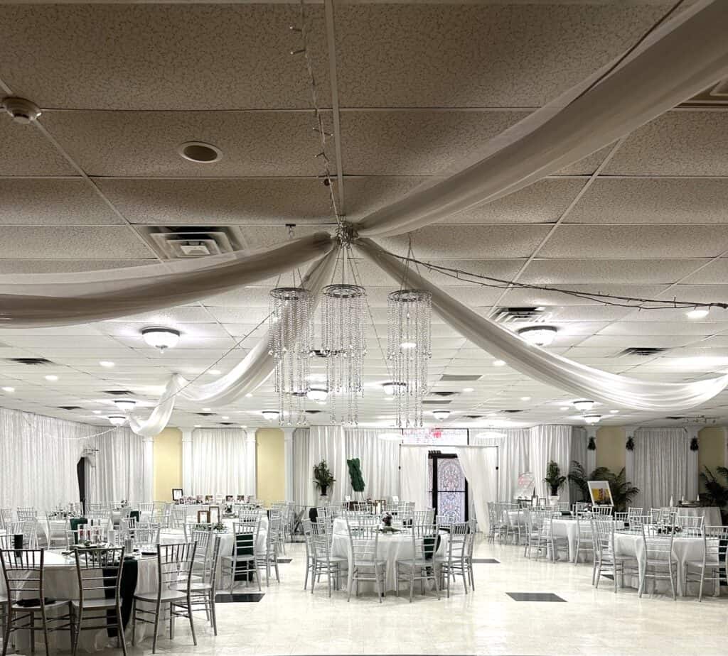 A banquet hall with white draped fabric on the ceiling, round tables with silver chairs, and minimal decorations.